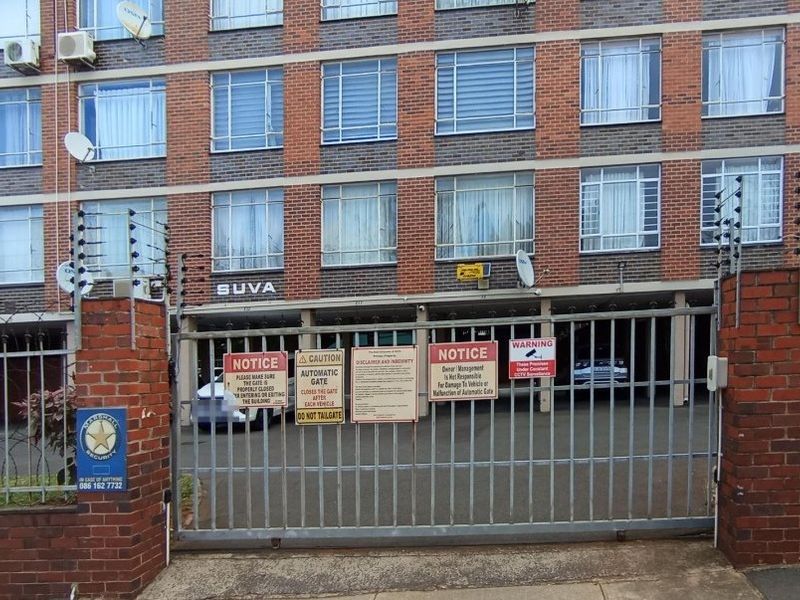 Front exterior view of the apartment building featuring a secure gated entrance, brick facade, and perimeter electric fencing.