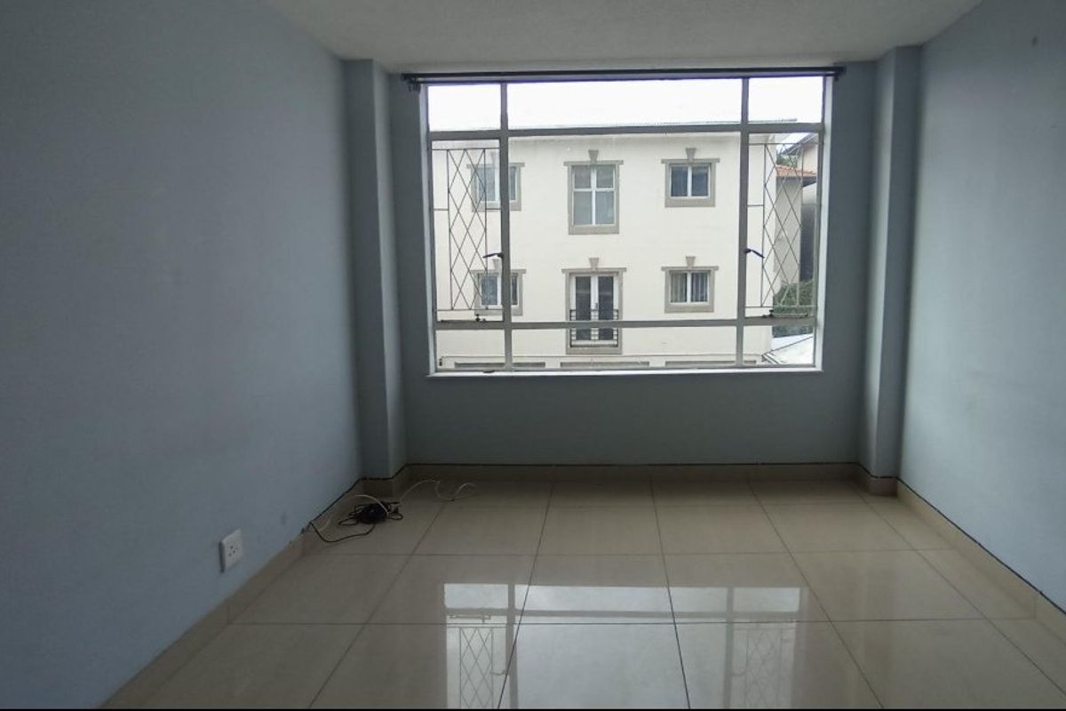 An empty bedroom featuring large windows with security bars and neutral tiled flooring, offering a bright and versatile living space.
