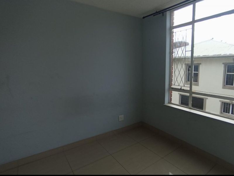 An empty bedroom featuring tiled flooring and a large window with security bars, offering a blank canvas for personalization.