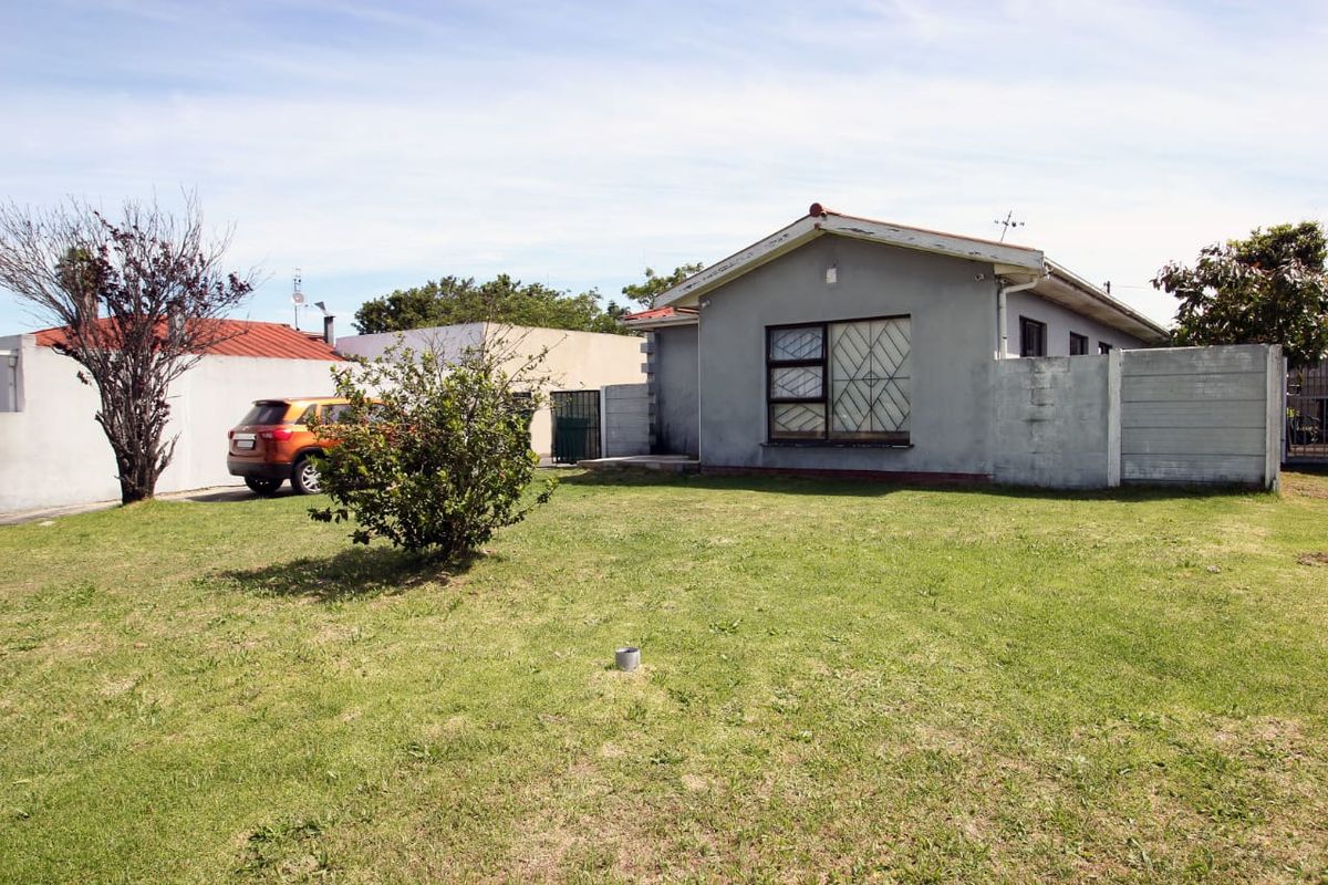 Rear view of the property featuring a lawn, precast concrete boundary wall, and a single-story house with security bars on the windows.