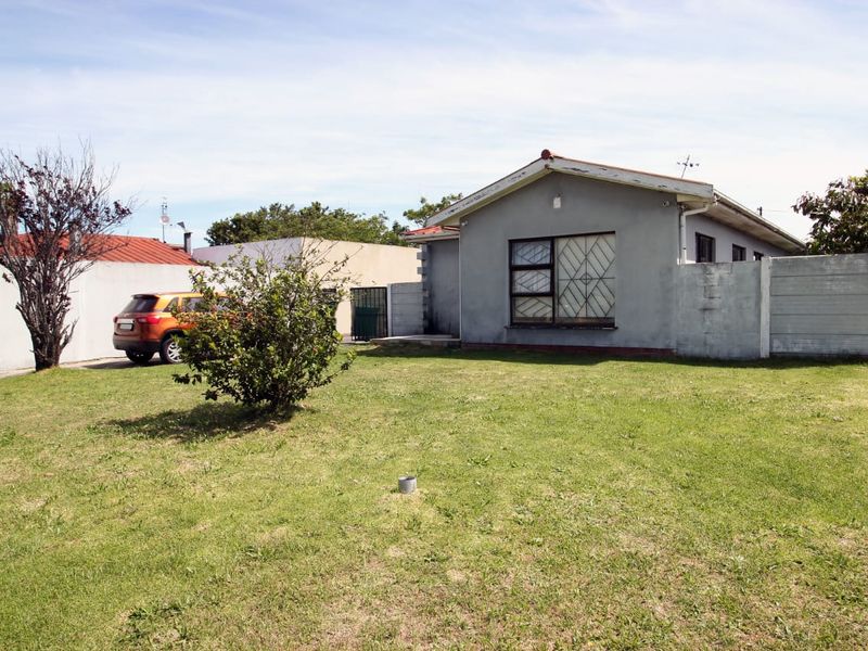 Rear view of the property featuring a lawn, precast concrete boundary wall, and a single-story house with security bars on the windows.