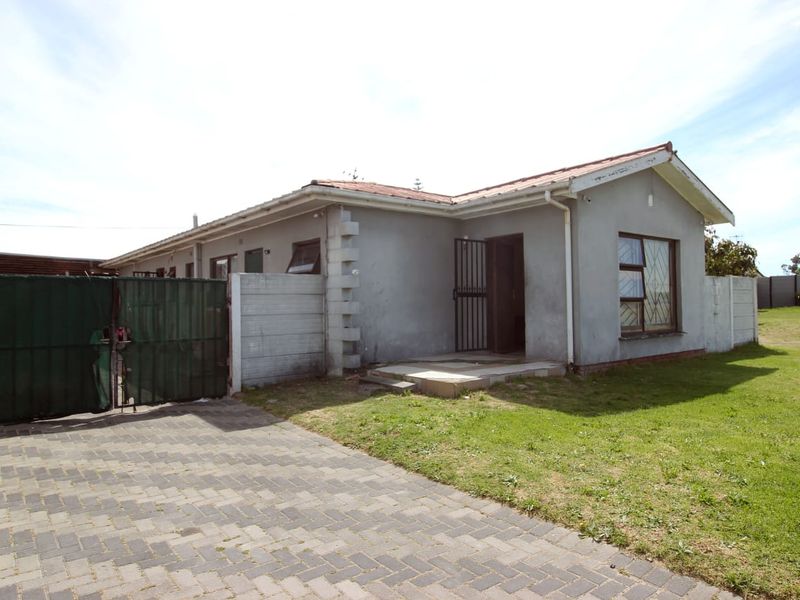 Front exterior view of a single-story house featuring a paved driveway, security gate, and precast boundary walling.