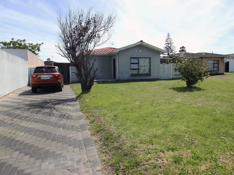 Front view of a single-story house featuring a paved driveway, a large front lawn, and a boundary wall.