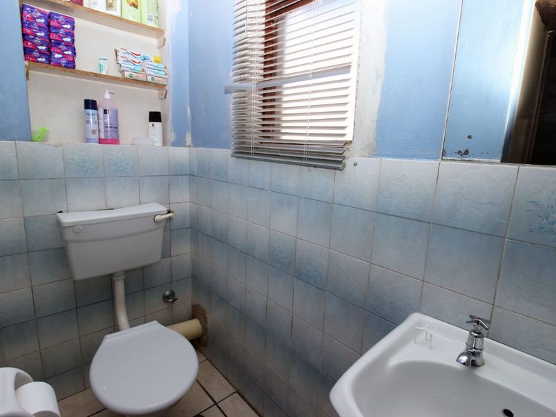 A compact bathroom featuring a standard toilet, washbasin, and tiled walls with built-in shelving, requiring cosmetic updates to the wall finishes and fixtures.