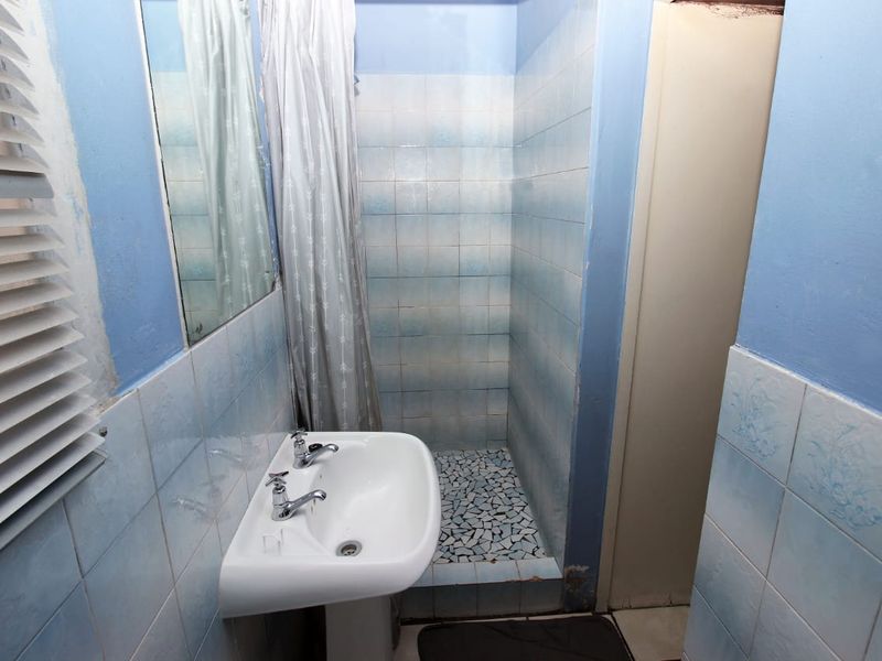 A functional bathroom featuring a pedestal washbasin and a tiled shower enclosure with dated blue ceramic wall finishes.