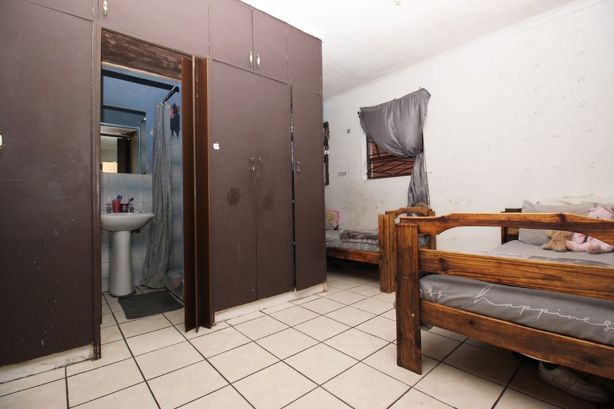 Bedroom featuring built-in cupboards, tiled flooring, and an en-suite bathroom with a pedestal basin. The room requires cosmetic updates to wall finishes and cabinetry.
