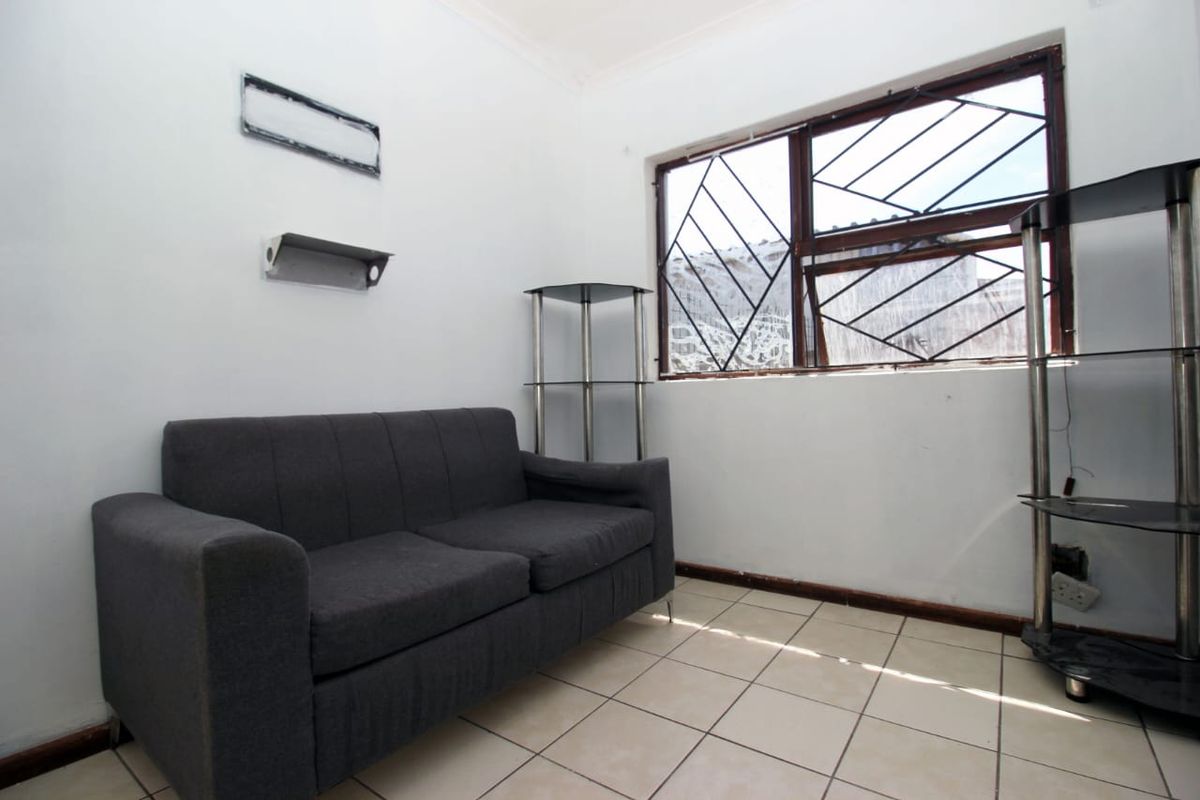 A compact living area featuring tiled flooring and a window with security bars, requiring some cosmetic updates to improve its overall appeal.