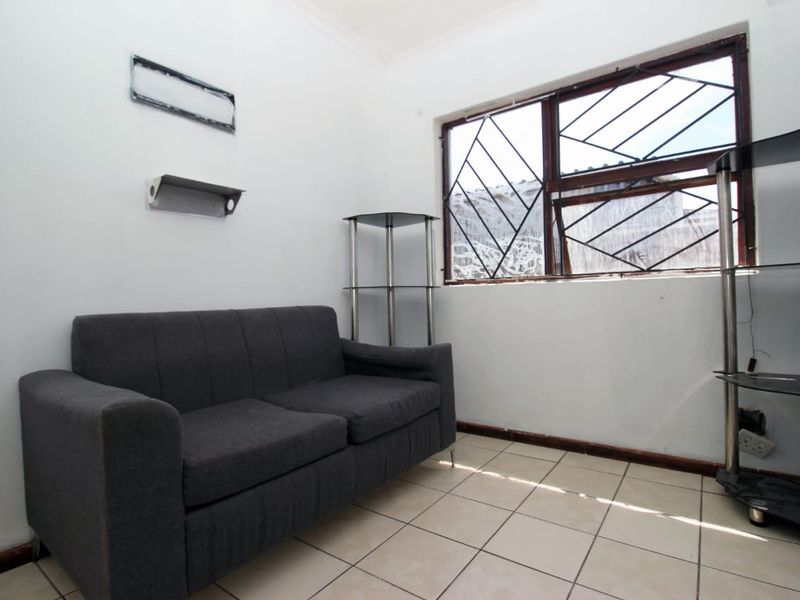 A compact living area featuring tiled flooring and a window with security bars, requiring some cosmetic updates to improve its overall appeal.