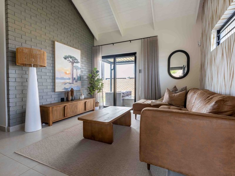 A bright living room featuring a vaulted ceiling with exposed rafters, a textured brick feature wall, and large sliding glass doors leading to the patio.