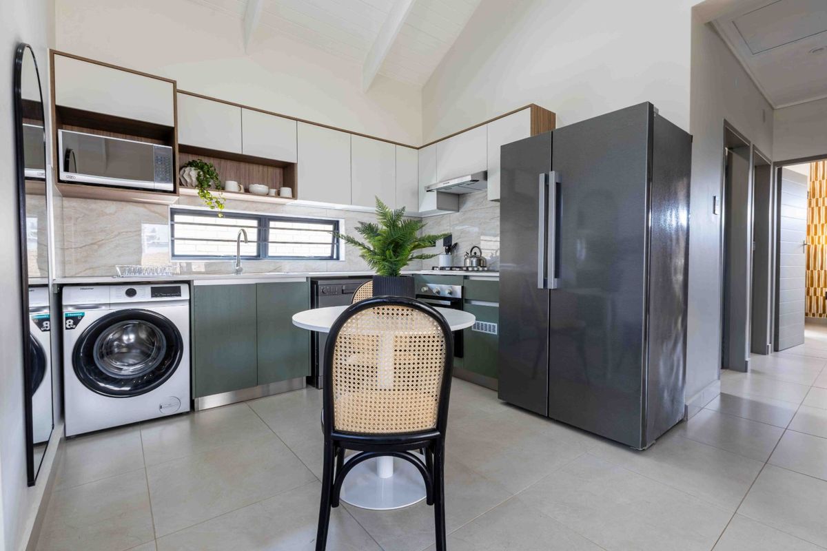 Modern kitchen featuring sleek two-tone cabinetry, stone-look backsplash, vaulted ceilings, and integrated appliances, offering a clean and contemporary aesthetic.