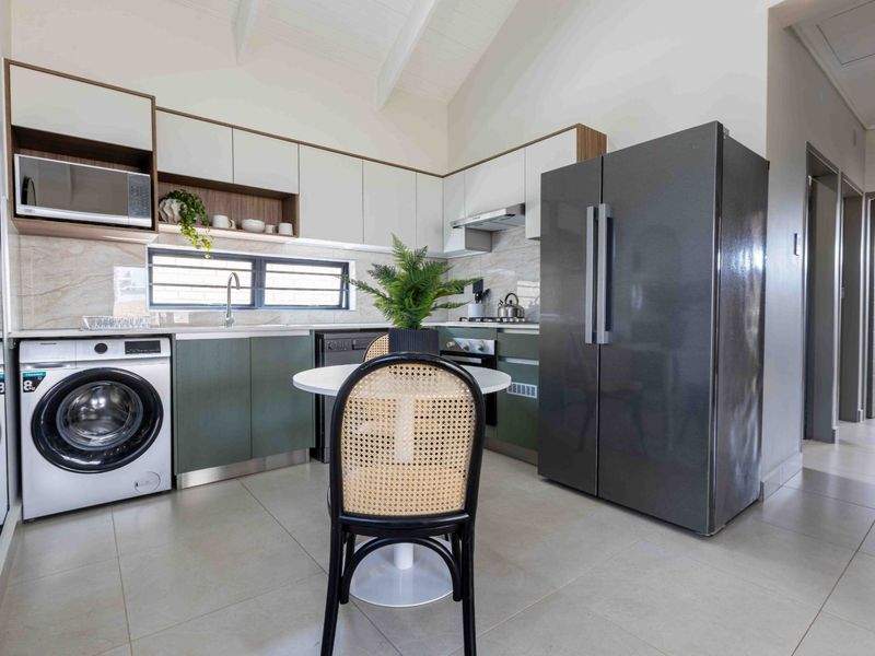 Modern kitchen featuring sleek two-tone cabinetry, stone-look backsplash, vaulted ceilings, and integrated appliances, offering a clean and contemporary aesthetic.
