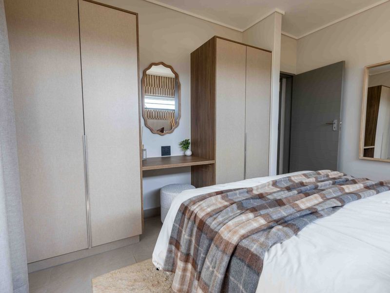 A well-appointed bedroom featuring modern built-in cupboards with an integrated vanity station and neutral finishes.