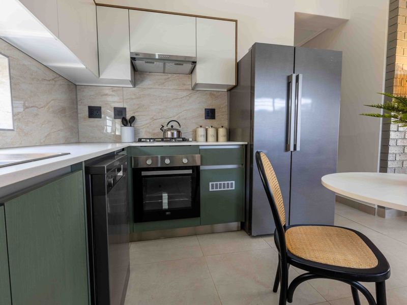 Modern kitchen featuring sleek green and white cabinetry, stone countertops, built-in oven, gas hob, and integrated appliances with a neutral tiled backsplash.