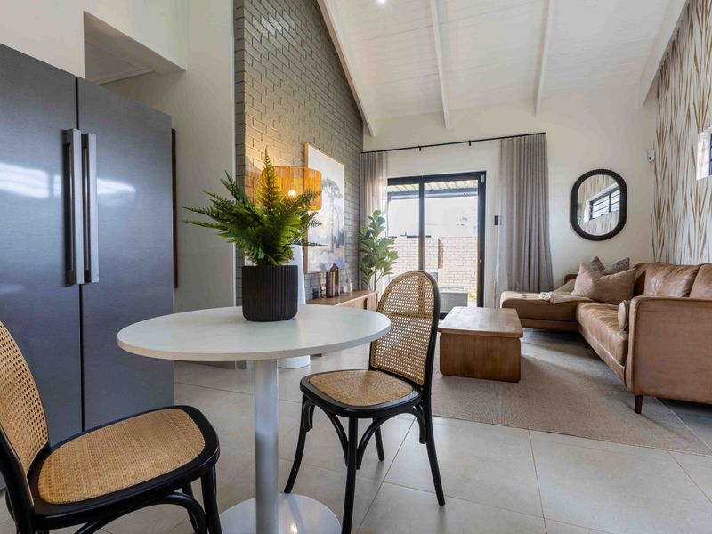 Bright open-plan living area featuring a vaulted ceiling with exposed rafters, a striking grey brick feature wall, and large sliding doors leading outdoors.