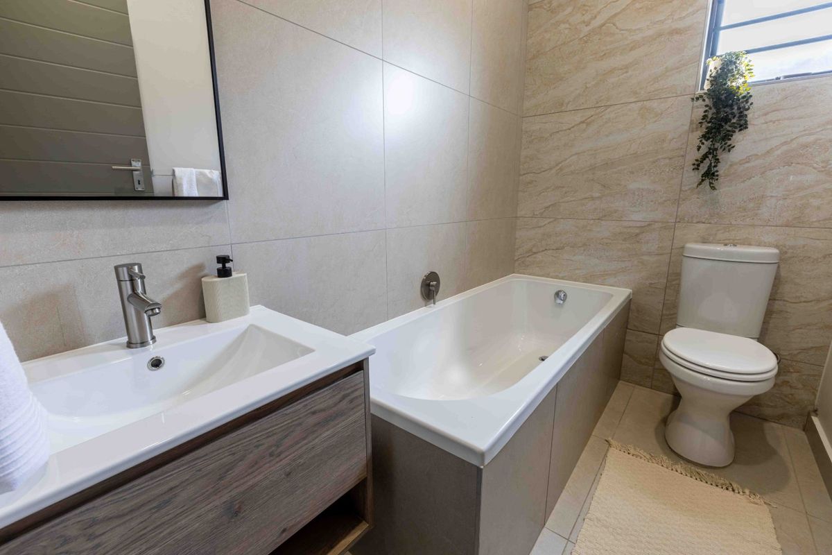 Modern bathroom featuring a vanity with basin, bathtub, and toilet, finished with neutral wall and floor tiles.