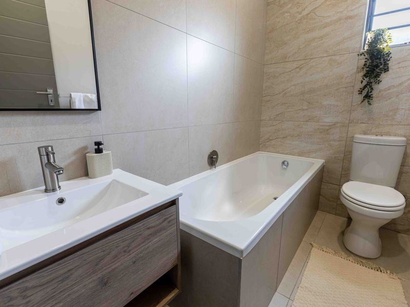 Modern bathroom featuring a vanity with basin, bathtub, and toilet, finished with neutral wall and floor tiles.
