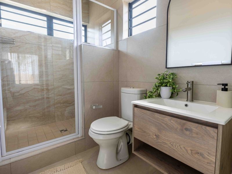 Modern bathroom featuring a walk-in shower with glass enclosure, a contemporary vanity with basin, and neutral wall tiling.