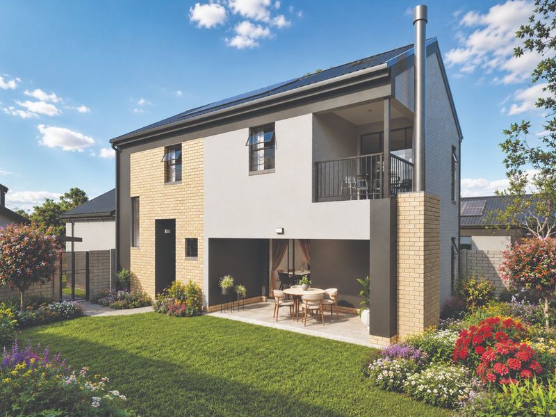 Rear view of a modern two-story house featuring a covered ground-floor patio, an upper-level balcony, external fireplace flue, and a well-maintained landscaped garden.