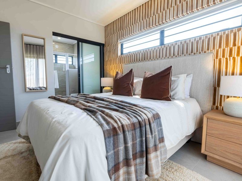 Modern bedroom featuring a textured feature wall, horizontal clerestory window, and an en-suite bathroom accessible via a sliding glass door.