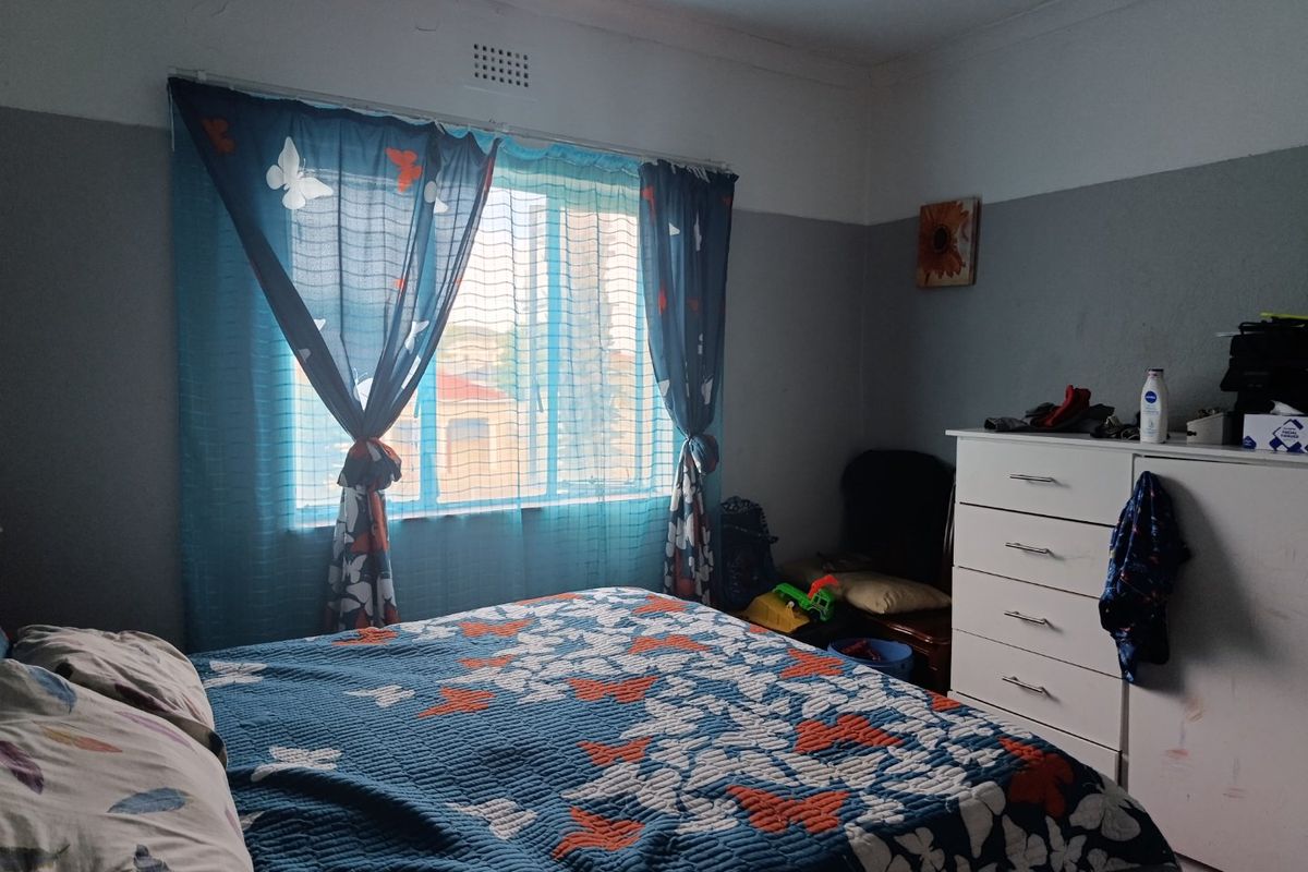 A bedroom featuring a window with natural light and a ventilation brick, showing signs of wear on the walls and ceiling.