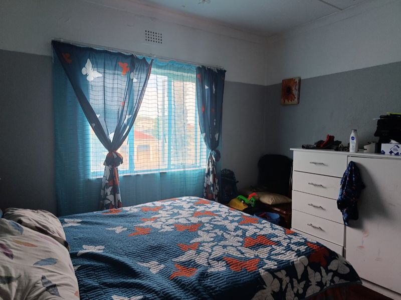 A bedroom featuring a window with natural light and a ventilation brick, showing signs of wear on the walls and ceiling.