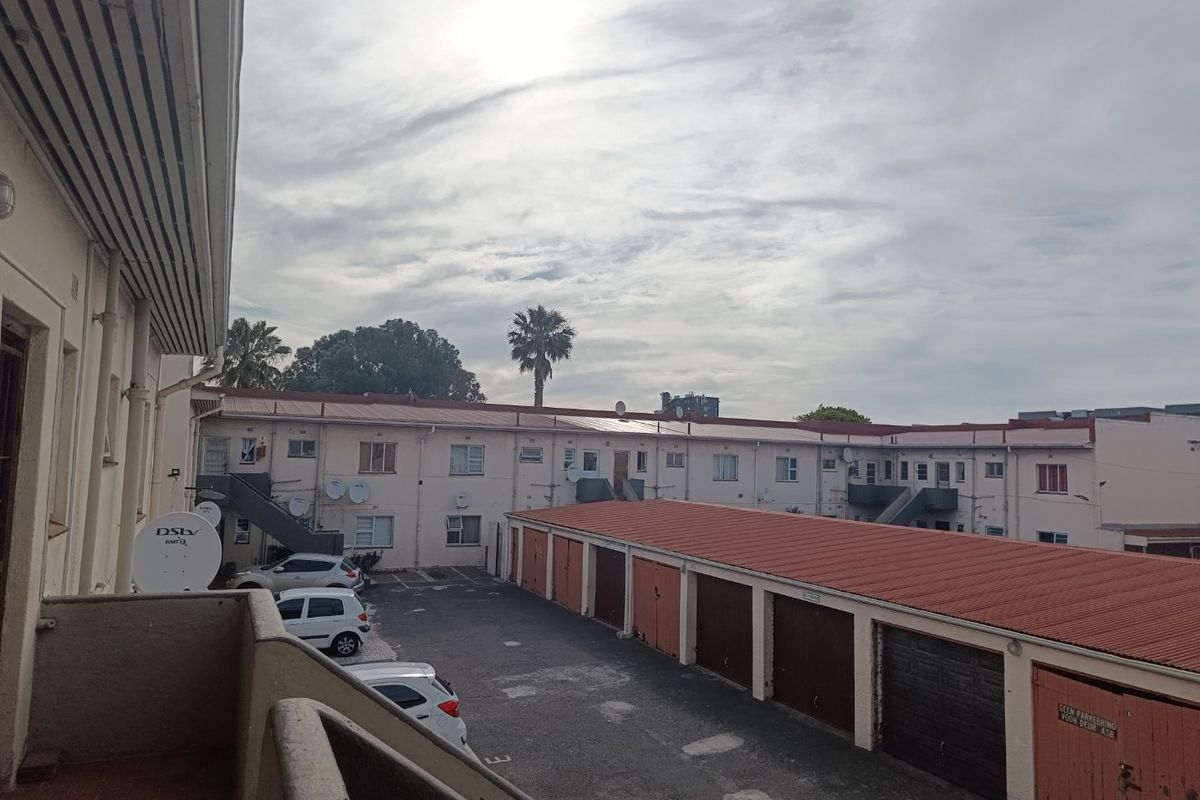View of the apartment complex rear courtyard featuring a row of garages, external staircases, and balcony access.