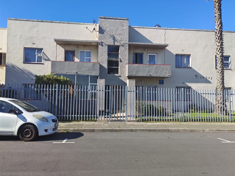 Front elevation of a multi-story apartment building featuring balconies, steel security fencing, and a central brick architectural feature.
