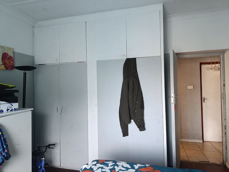 A bedroom featuring built-in cupboards with overhead storage and classic cove cornice detailing, requiring cosmetic updates to improve the overall aesthetic.