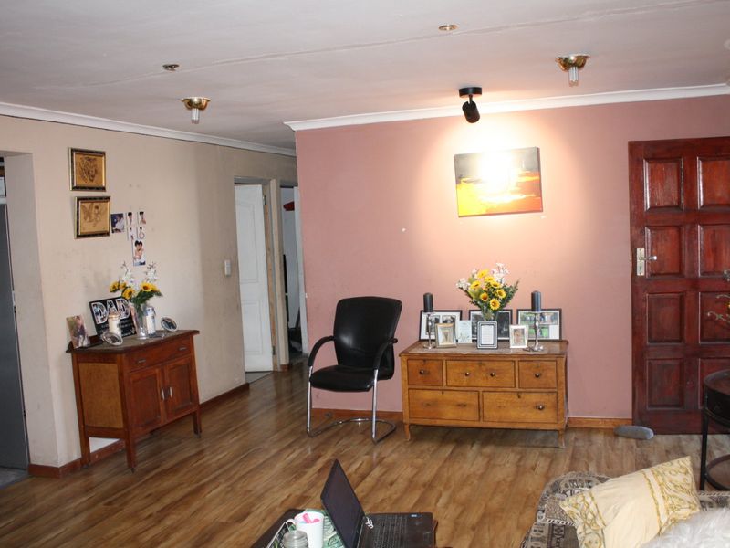 A living room featuring laminate flooring, recessed lighting, and a timber panel door, requiring cosmetic updates to the walls and ceiling.