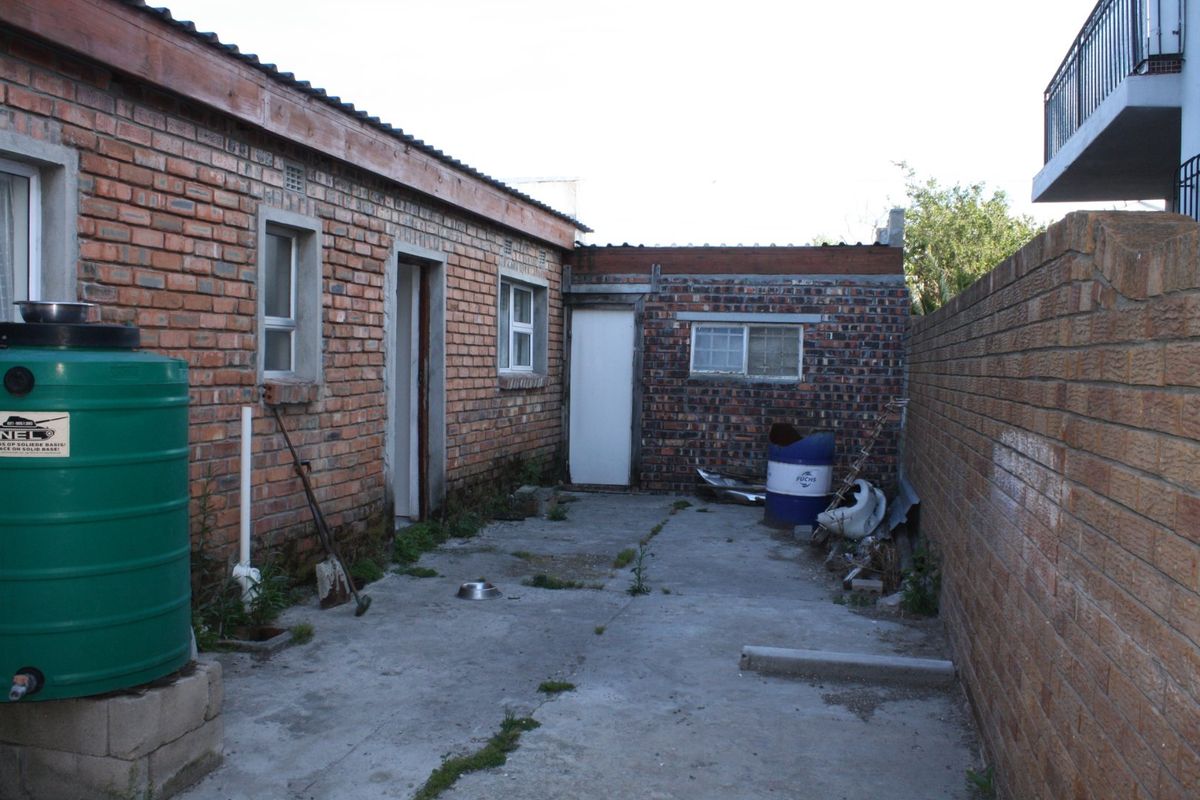 Rear exterior area featuring exposed brick walls, concrete paving, and a water storage tank, showing signs of wear and maintenance requirements.