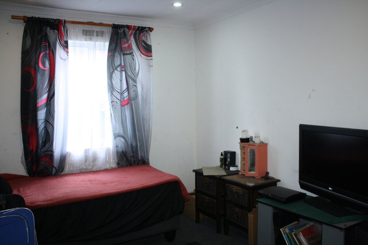 A compact bedroom featuring a window with curtains and recessed ceiling lighting, requiring minor cosmetic updates to the wall finishes.