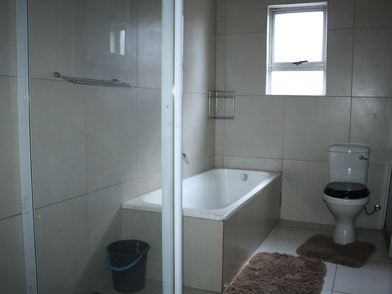 A functional bathroom featuring a built-in bathtub, separate shower enclosure, and toilet with neutral wall and floor tiling.