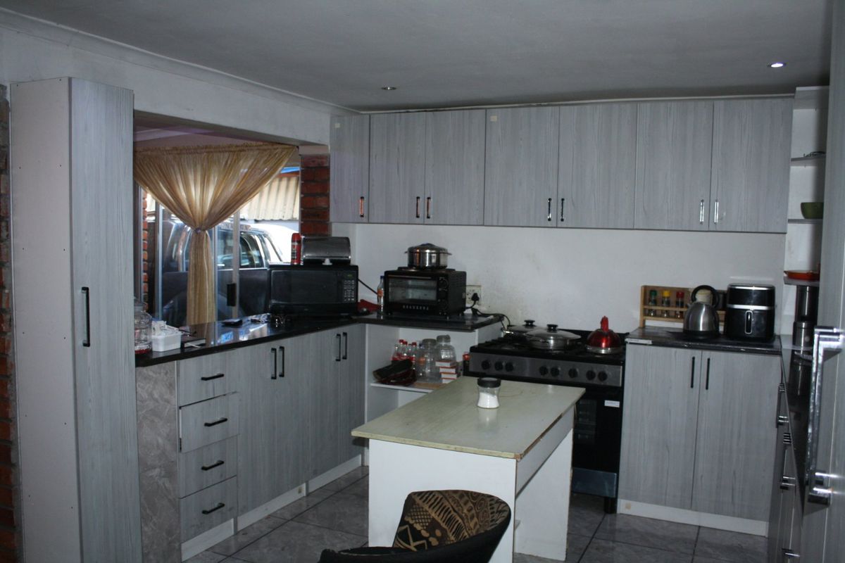 A functional kitchen featuring light-toned cabinetry, laminate countertops, tiled flooring, and a freestanding stove, offering a practical layout for daily meal preparation.