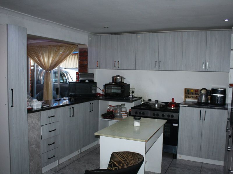 A functional kitchen featuring light-toned cabinetry, laminate countertops, tiled flooring, and a freestanding stove, offering a practical layout for daily meal preparation.