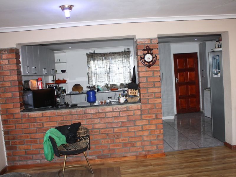 Open plan living area featuring an exposed brick breakfast bar, laminate flooring, and direct access to a tiled hallway with a solid wood door.