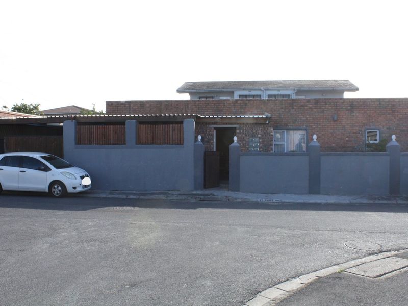 Front elevation of a brick house featuring a perimeter wall, gated entrance, and a covered carport area.