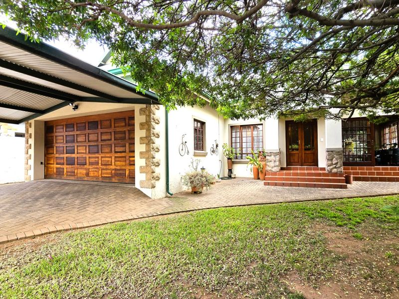 Front elevation of the house featuring a paved driveway, covered carport, wooden garage door, and a welcoming entrance with tiled steps and stone accents.