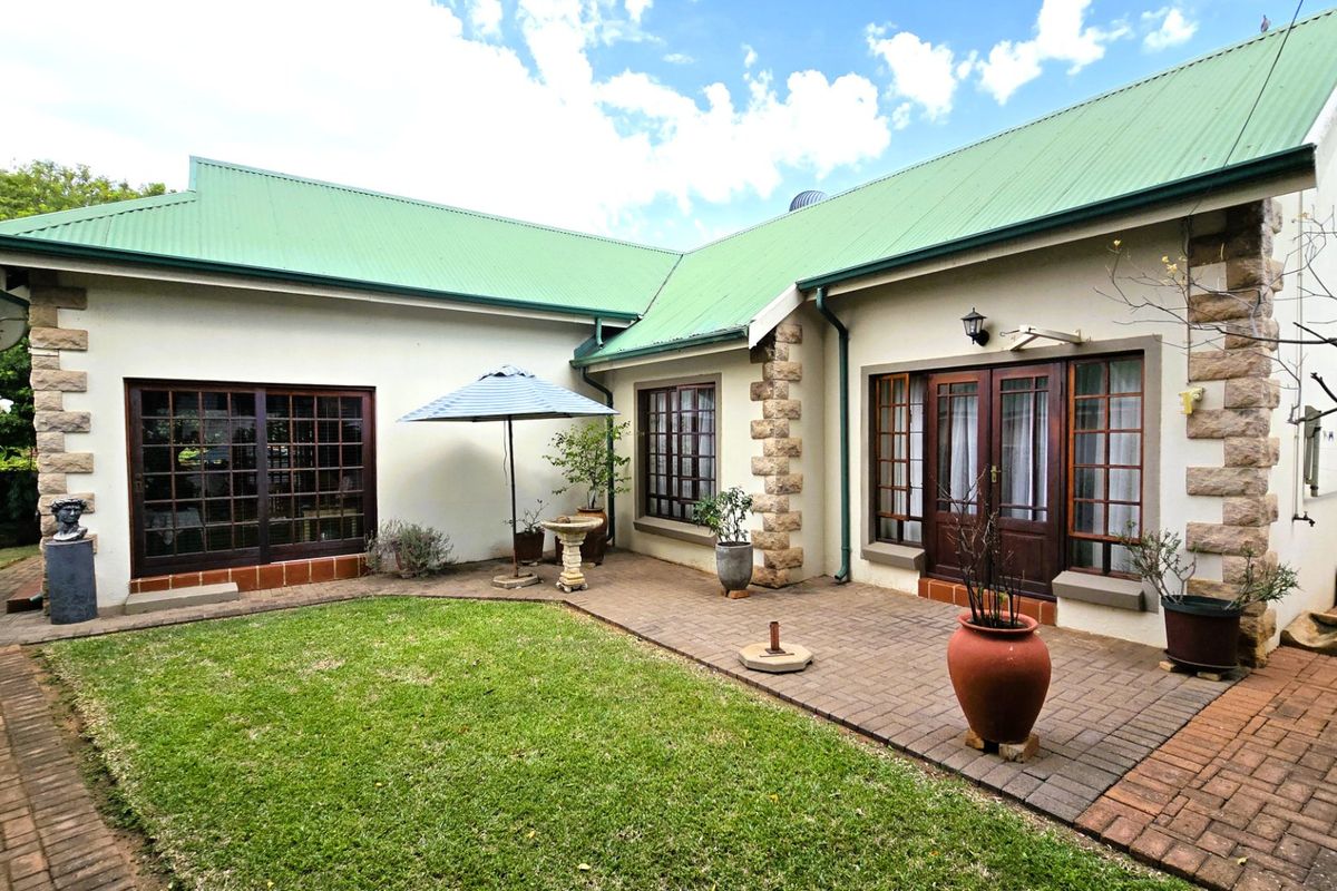 Rear view of the house featuring a paved patio area, green metal roof, stone detailing, and timber-framed doors leading into the home.