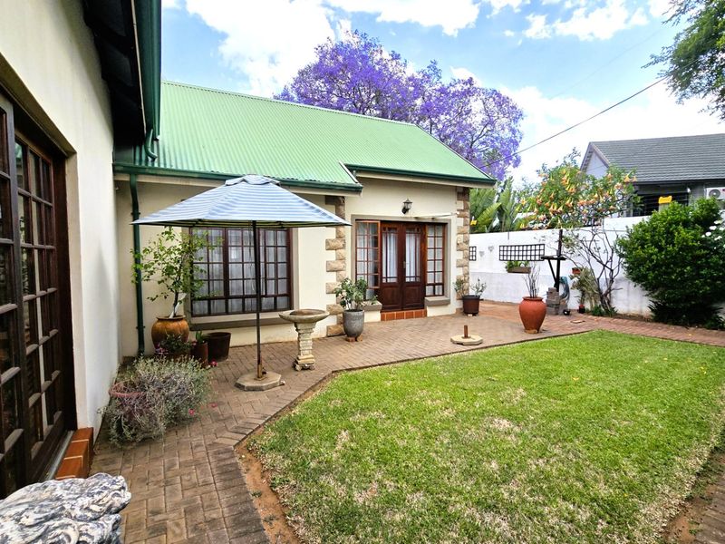 A well-maintained rear garden featuring a brick-paved patio area, stone-clad accents, and a green corrugated metal roof.