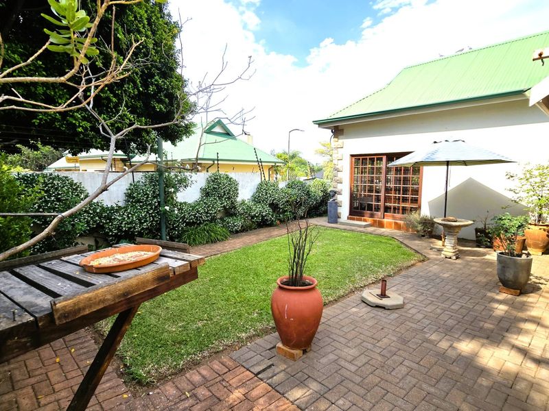 A private rear garden featuring a paved patio area, a well-maintained lawn, and stone-clad exterior walls with timber-framed access doors.