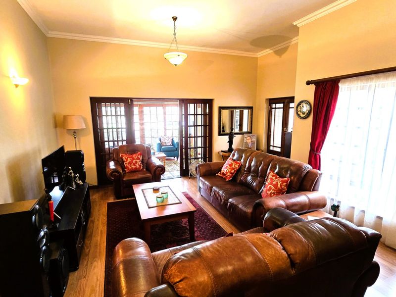 A comfortable living room featuring laminate flooring, cove cornicing, and double french doors leading to an adjacent space.