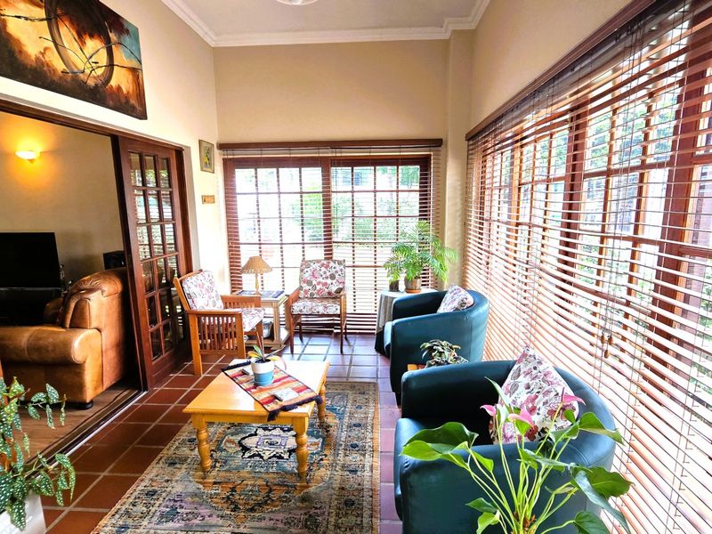 A sun-drenched enclosed patio featuring terracotta tiled flooring, extensive wooden-framed windows with venetian blinds, and direct access to the adjacent living area.