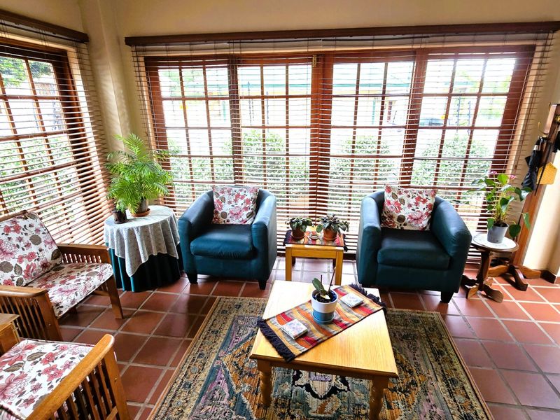 A sunlit enclosed patio featuring terracotta floor tiles and large timber-framed glass doors with venetian blinds, offering a bright and inviting transition space.