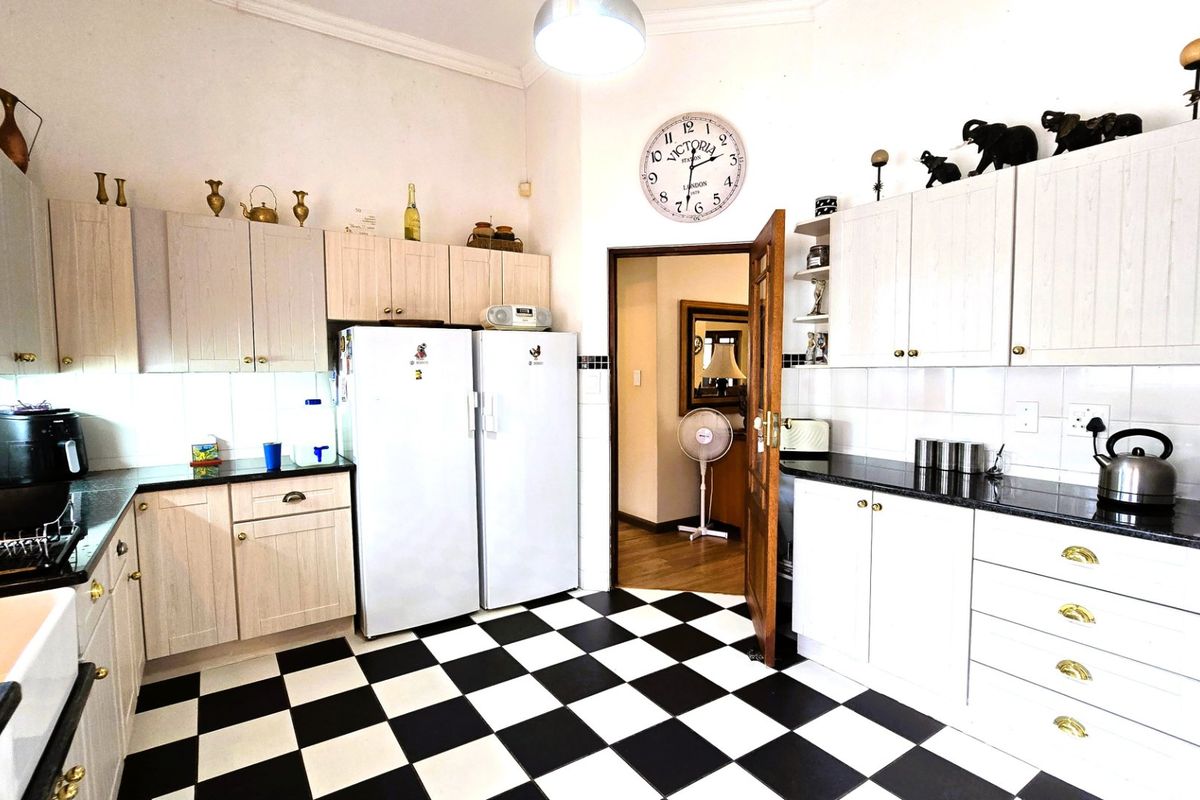 A functional kitchen featuring light-toned built-in cabinetry, dark granite countertops, a classic checkerboard tiled floor, and a traditional apron-front sink.