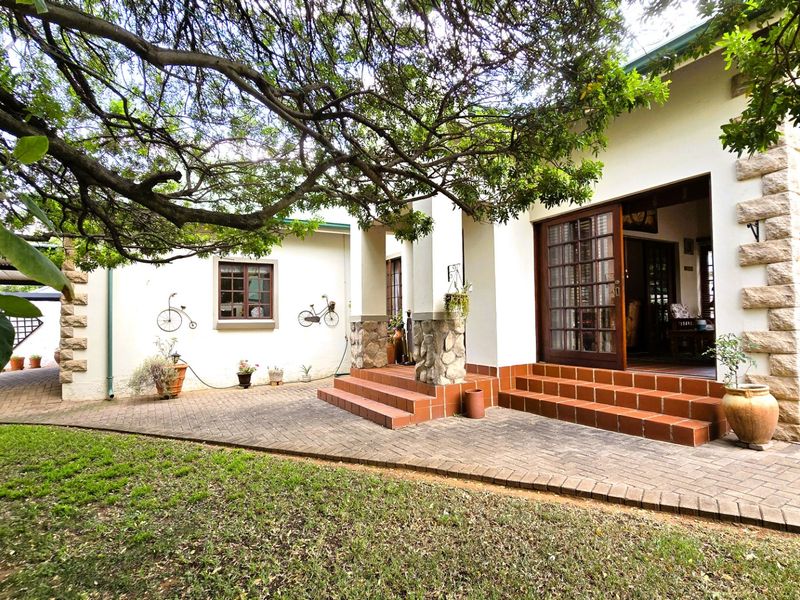 A charming rear exterior view featuring a paved patio, stone-clad accents, and timber-framed glass doors leading into the home.