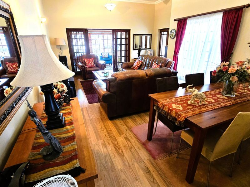 Spacious open-plan living and dining area featuring laminate flooring, large windows with curtains, and french doors leading to an outdoor space.