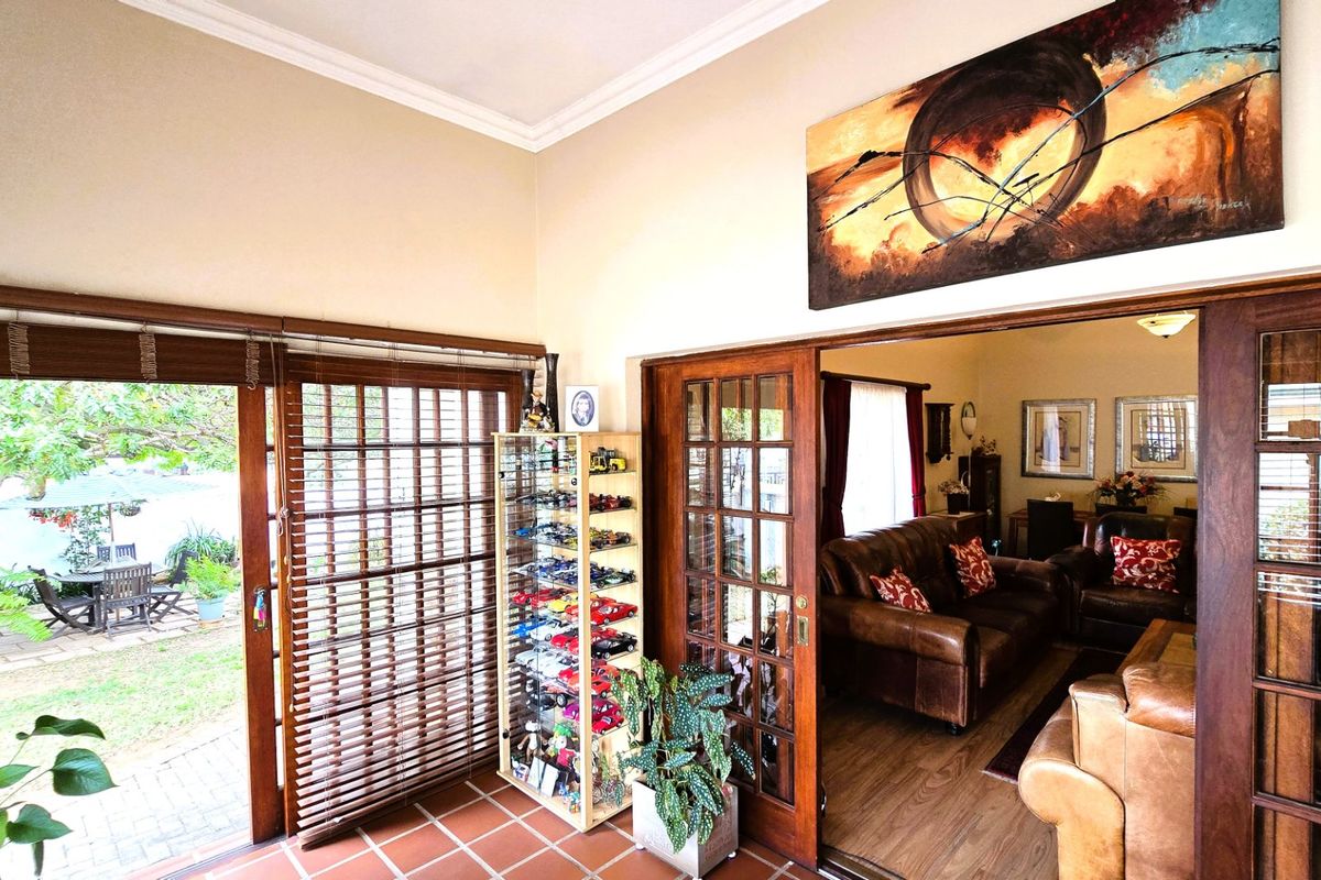 A bright living area featuring terracotta floor tiles, crown molding, and wooden sliding doors that provide seamless access to the outdoor patio area.