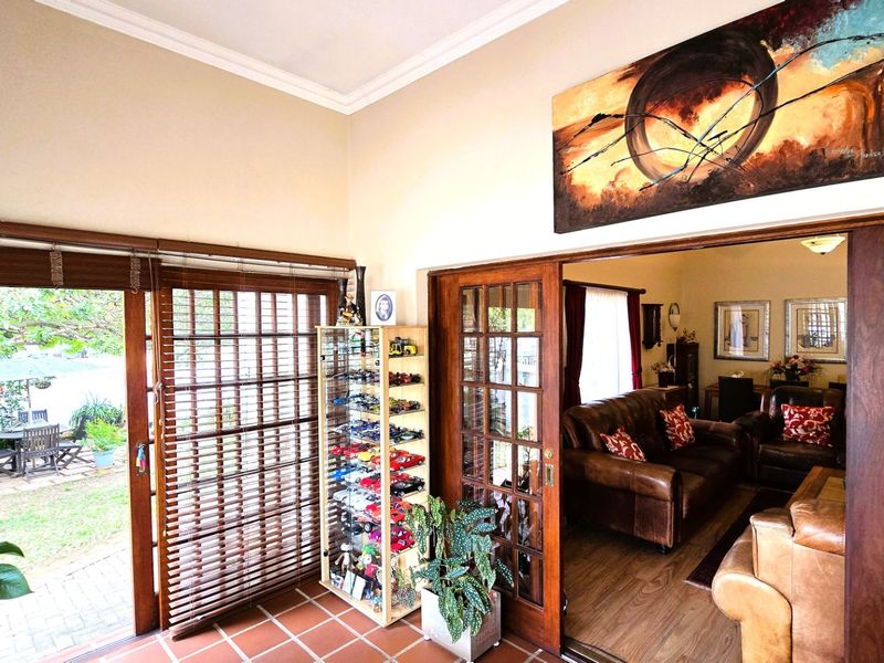 A bright living area featuring terracotta floor tiles, crown molding, and wooden sliding doors that provide seamless access to the outdoor patio area.