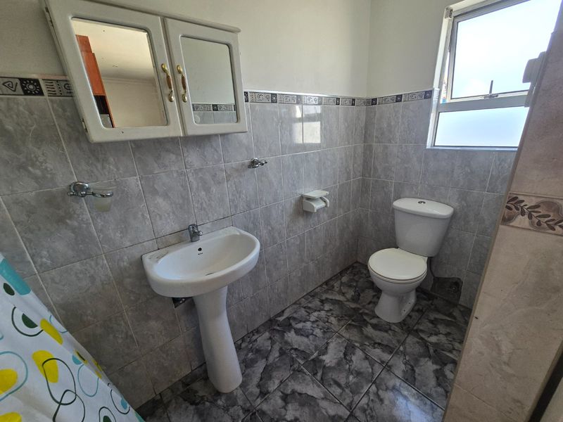 A functional bathroom featuring a pedestal basin, toilet, and wall-mounted medicine cabinet, finished with neutral wall and floor tiling.