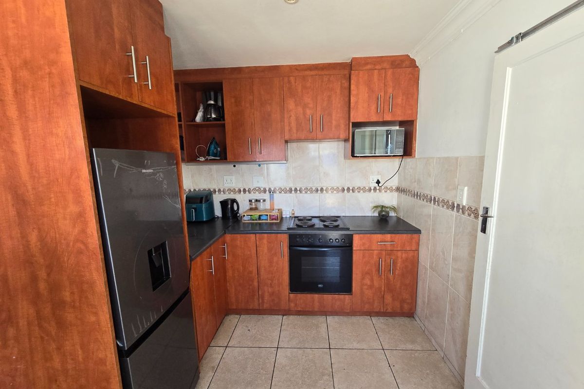A functional kitchen featuring wooden cabinetry, laminate countertops, a built-in oven with electric hob, and tiled flooring.